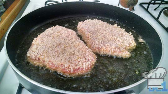 Breaded pork chops searing in a pan of oil.