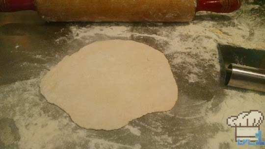 Roti bread dough rolled out flat with rolling pin on floured surface.