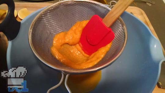 Pushing the soup through a fine sieve with a rubber spatula to filter it free of the large chunks and make the soup a smooth consistency.
