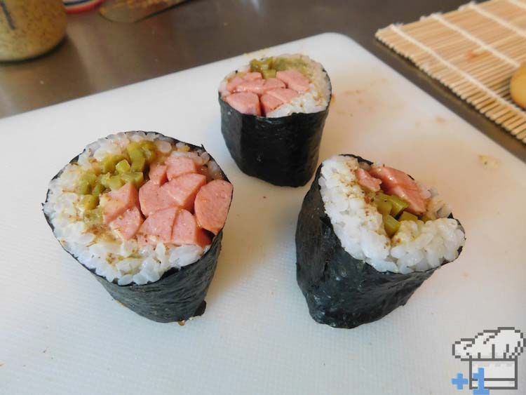 Sliced hot dog sushi rolls resting on mat, awaiting the buns.