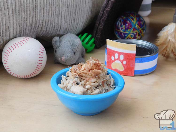 A bowl of the finished recipe of Bonito Bitz cat food, among an array of various cat toys.