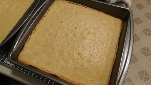 A pan of freshly baked almond genoise cake removed from the oven and cooling before slicing.