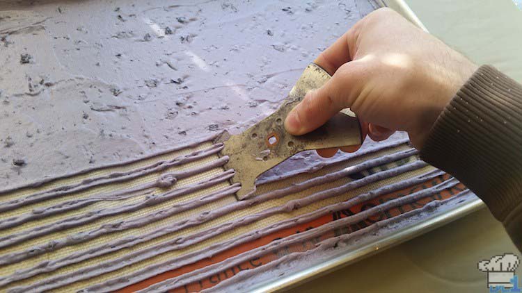 Creating striped lines in the blueberry joconde sponge cake batter by scraping a grooved instrument over the top of the batter before baking.