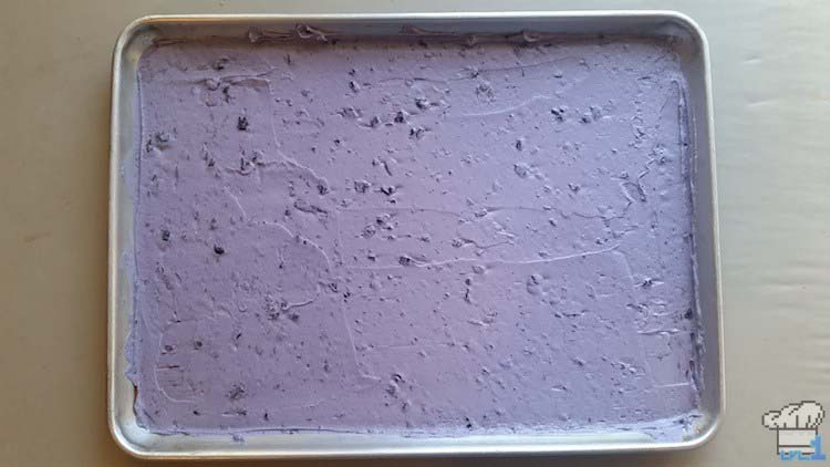 Blueberry joconde sponge cake batter spread evenly in the basin of a shallow small rectangular baking tray.