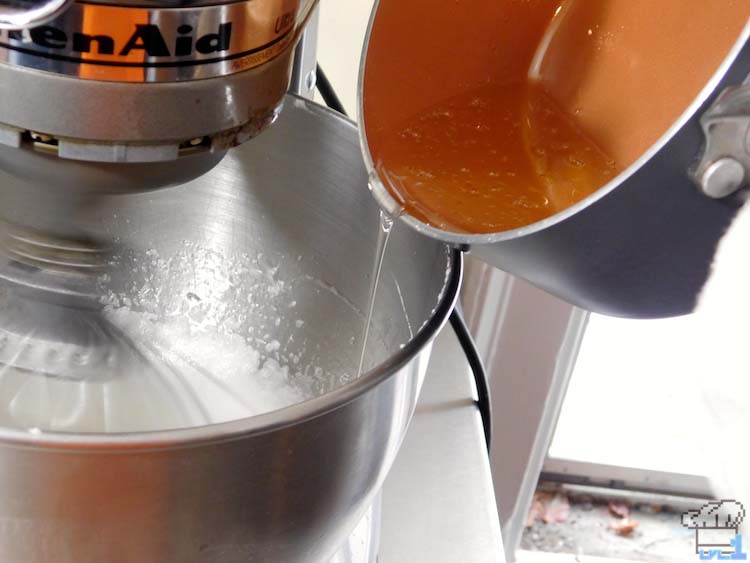 Slowly pouring the hot sugar into the whipping egg whites to temper them for a stiff meringue.