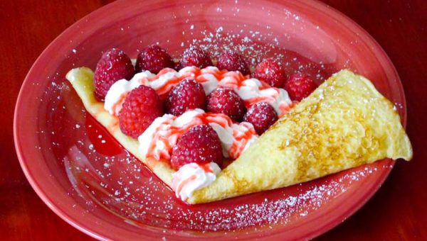 Finished wild berry crepes garnished with fresh raspberries, whipped cream and powdered sugar, from the Legend of Zelda Breath of the Wild game series.